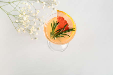 Glass of tasty grapefruit cocktail and flowers on gray backgroundの写真素材