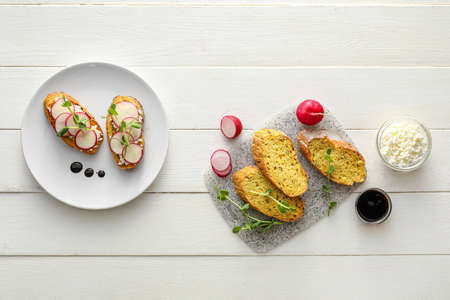 Tasty bruschettas with cheese, radish and ingredients on light wooden backgroundの写真素材