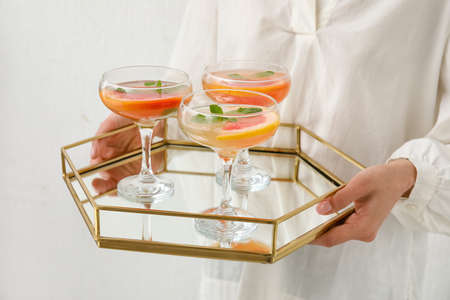 Woman holding tray with glasses of tasty grapefruit cocktail on light background, closeup