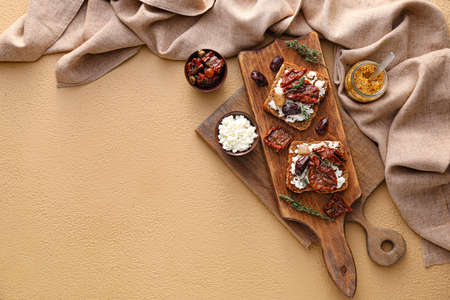 Tasty bruschettas with cheese, sun-dried tomatoes and dates on color background