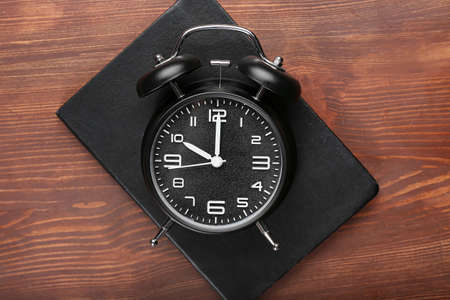 Stylish alarm clock with notebook on dark wooden background