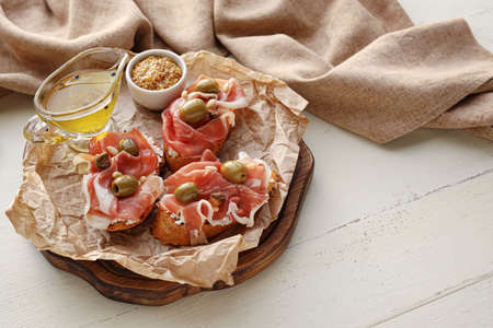Tasty bruschettas with prosciutto, olives, oil and Dijon mustard on light wooden backgroundの写真素材