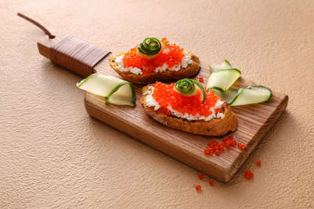 Tasty bruschettas with cheese, red caviar and cucumber on color backgroundの写真素材