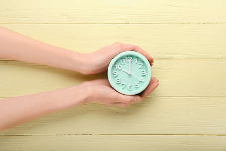 Female hands and alarm clock on color wooden backgroundの写真素材