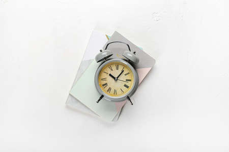 Stylish alarm clock with notebooks on white background