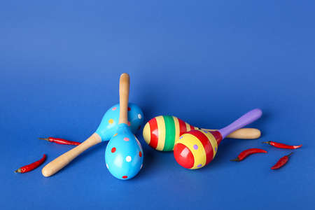Mexican maracas and chili peppers on color background