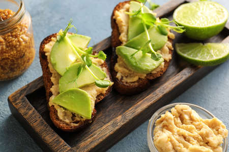 Tasty bruschettas with avocado, hummus and mustard on color background, closeup