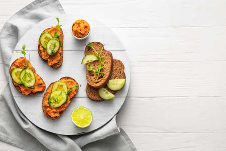 Tasty bruschettas with cucumber on white wooden background