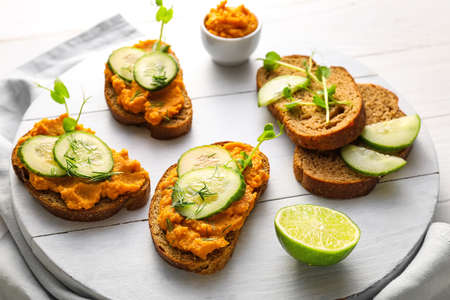 Tasty bruschettas with cucumber on white wooden background
