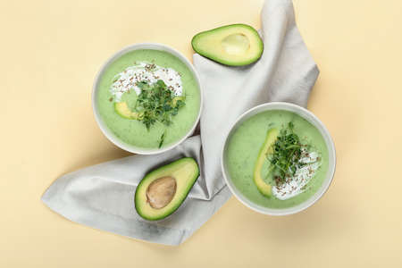 Bowls with green gazpacho and avocado on color background