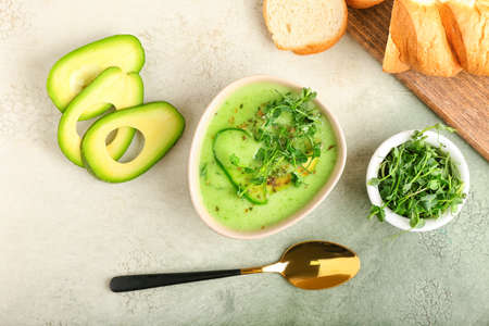 Bowl with green gazpacho and ingredients on color background