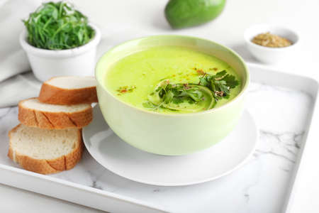 Tray with green gazpacho and ingredients on light background