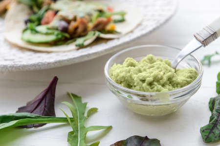 Tasty guacamole in bowl on light wooden background, closeup