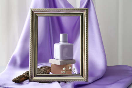 Composition with stylish bottle of perfume and frame on color cloth background