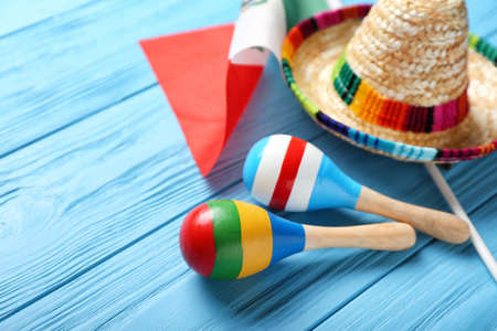 Mexican flag, maracas and sombrero on color wooden background