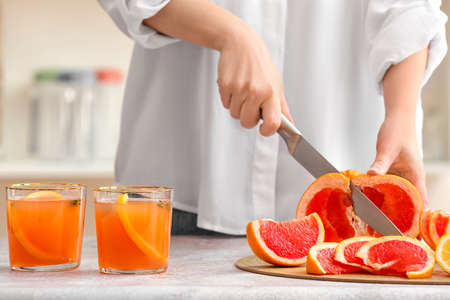 Woman cutting grapefruit on table in kitchenの写真素材