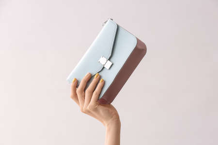 Female hand with beautiful manicure and bag on light background