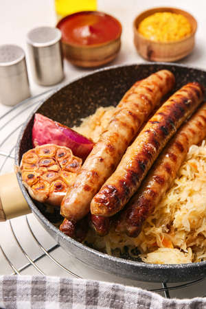 Frying pan with tasty sauerkraut and grilled sausages on light background, closeupの写真素材