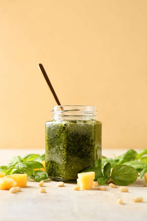 Jar with fresh pesto sauce and ingredients on table