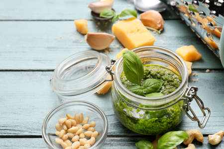 Jar with fresh pesto sauce and ingredients on color wooden backgroundの写真素材