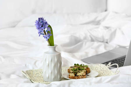 Tray with hyacinth flower and tasty breakfast on bed