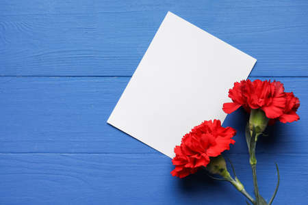 Fresh carnation flowers with empty paper sheet on color wooden backgroundの写真素材