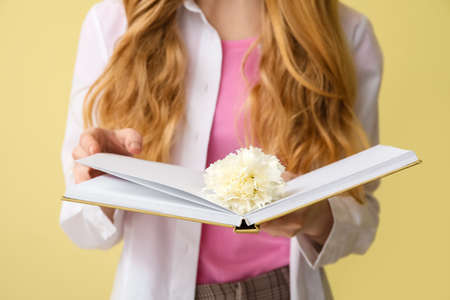 Young woman with beautiful carnation flower and book on color background