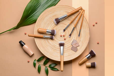 Set of makeup brushes with decorative cosmetics on color background
