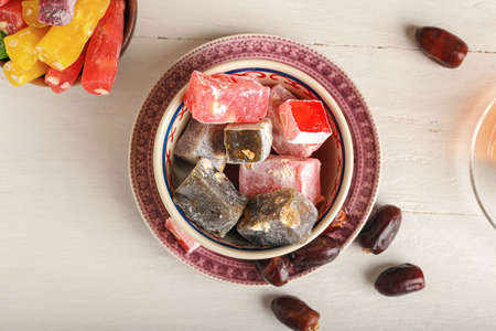 Bowl with tasty Turkish delight and dried dates on white wooden background