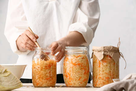 Woman taking tasty sauerkraut from glass jar at table in kitchen, closeup