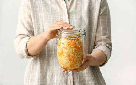 Woman with glass jar of tasty sauerkraut on light background, closeupの写真素材