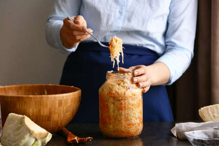 Woman tasty sauerkraut in glass jar on table putting at kitchen, closeupの写真素材