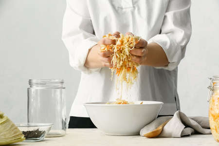 Woman preparing tasty sauerkraut at table in kitchen, closeup