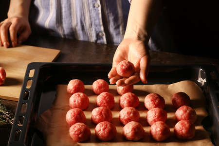 Woman tasty cutlets made of fresh putting forcemeat in baking tray at table, closeup