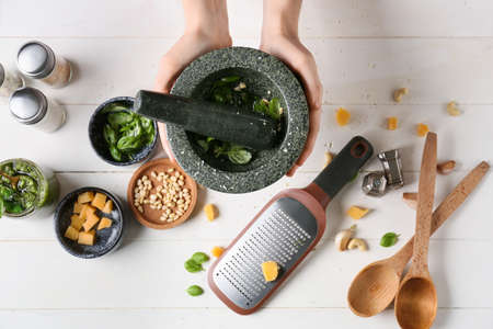 Woman preparing tasty pesto sauce on light wooden background