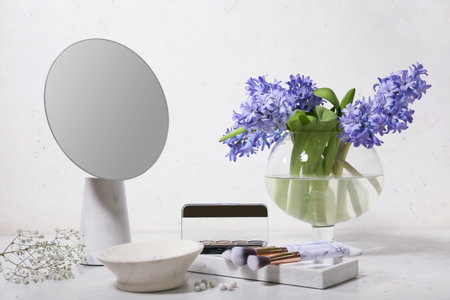 Vase with bouquet of beautiful hyacinth flowers, mirror and cosmetics on tableの写真素材