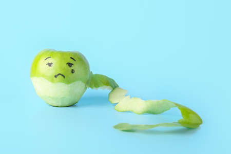 Composition with peeled apple with drawn sad face on blue backgroundの写真素材