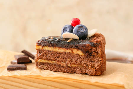 Board with delicious piece of chocolate cake and berries on light background