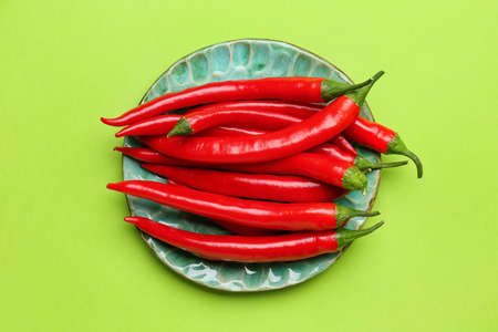 Plate with hot chili peppers on green background