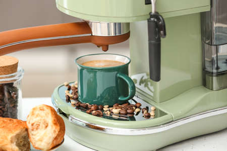Modern machine with cup of fresh coffee on table in kitchenの写真素材