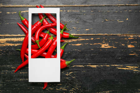 Blank frame and hot chili peppers on dark wooden backgroundの写真素材