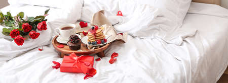 Tray with tasty breakfast, rose flowers and gift on bed. Valentine's Day celebrationの写真素材