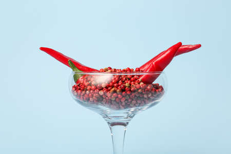 Glass with hot chili peppers and peppercorns on blue backgroundの写真素材