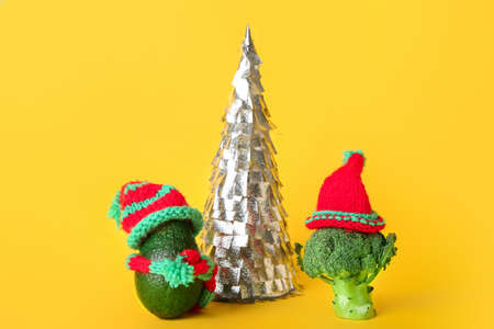 Composition with Christmas tree, avocado and broccoli in knitted hats on yellow backgroundの写真素材