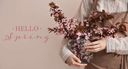Woman with beautiful blossoming tree branches in vase on color background. hello springの写真素材