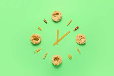 Clock made of raw pasta on green backgroundの写真素材