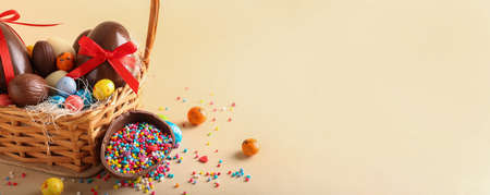 Basket with chocolate Easter eggs, candies and sprinkles on beige background with space for textの写真素材