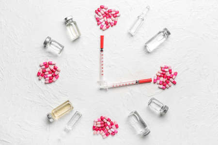 Clock made of pills, ampules and syringes on light background