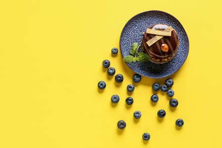 Plate with delicious chocolate cake and blueberries on yellow background