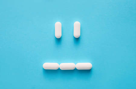 Sad face made of pills on color background